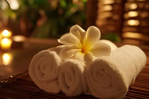 Neatly rolled white towels with frangipani flower in a serene spa setting at DLUX Health & Beauty Centre