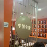 Interior view of a Chinese restaurant with orange walls and traditional opera mask decorations, sign reads '中国名堂'