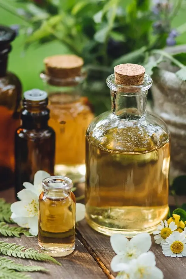 essential-oil-bottles-outdoor-flower Glass bottles of essential oils with chamomile and jasmine flowers on a wooden table outdoors